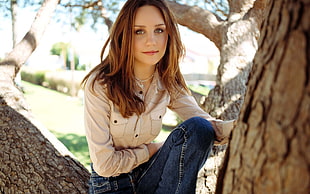 woman wearing beige button-up long-sleeved shirt and blue jeans sitting on tree